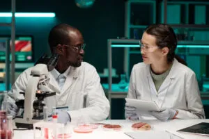 Two scientists in lab coats examining cultured meat samples and petri dishes in a laboratory, representing research in lab-grown meat and food technology.